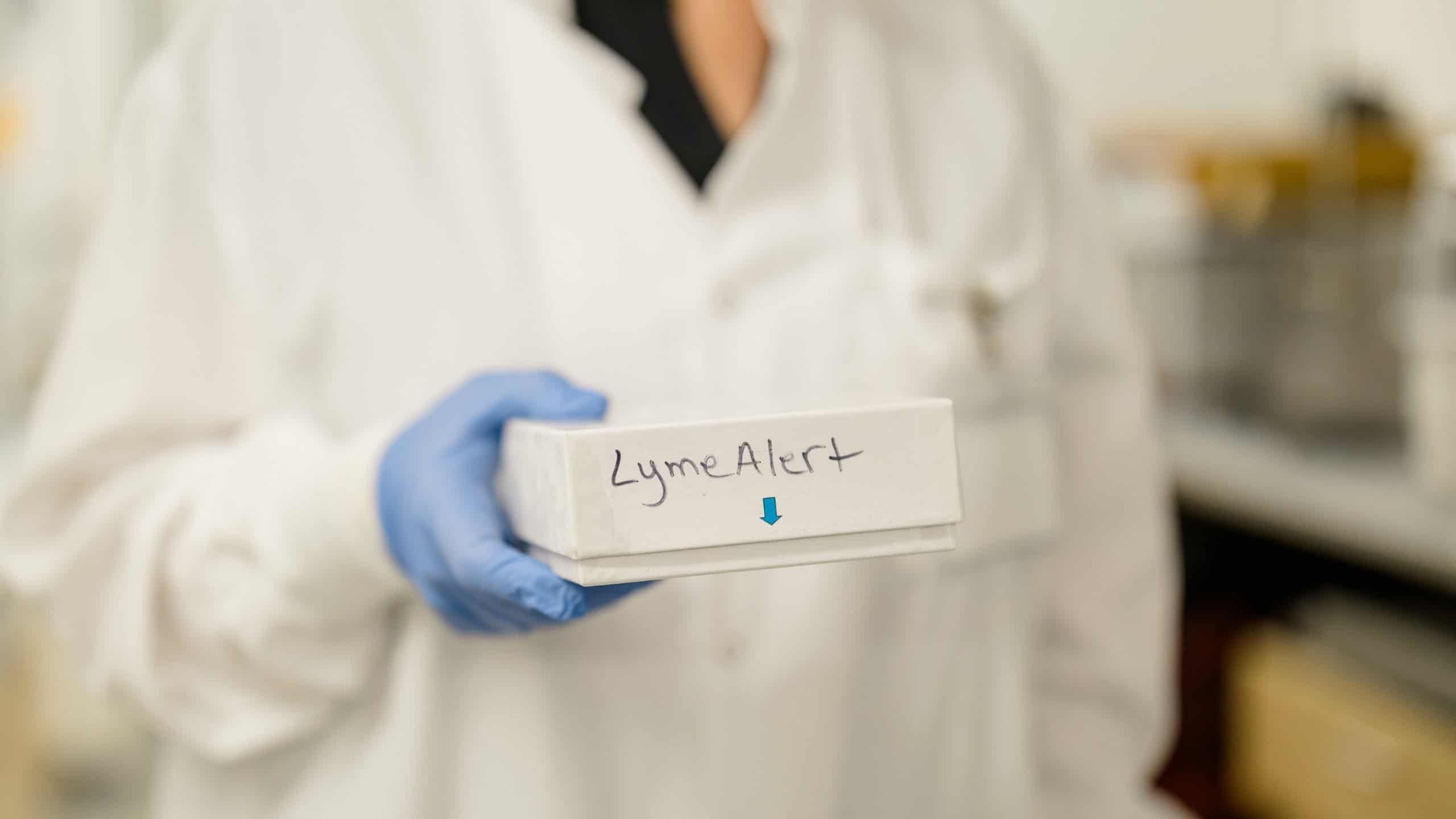 Person holding a Lyme disease test kit with handwritten label "LymeAlert".